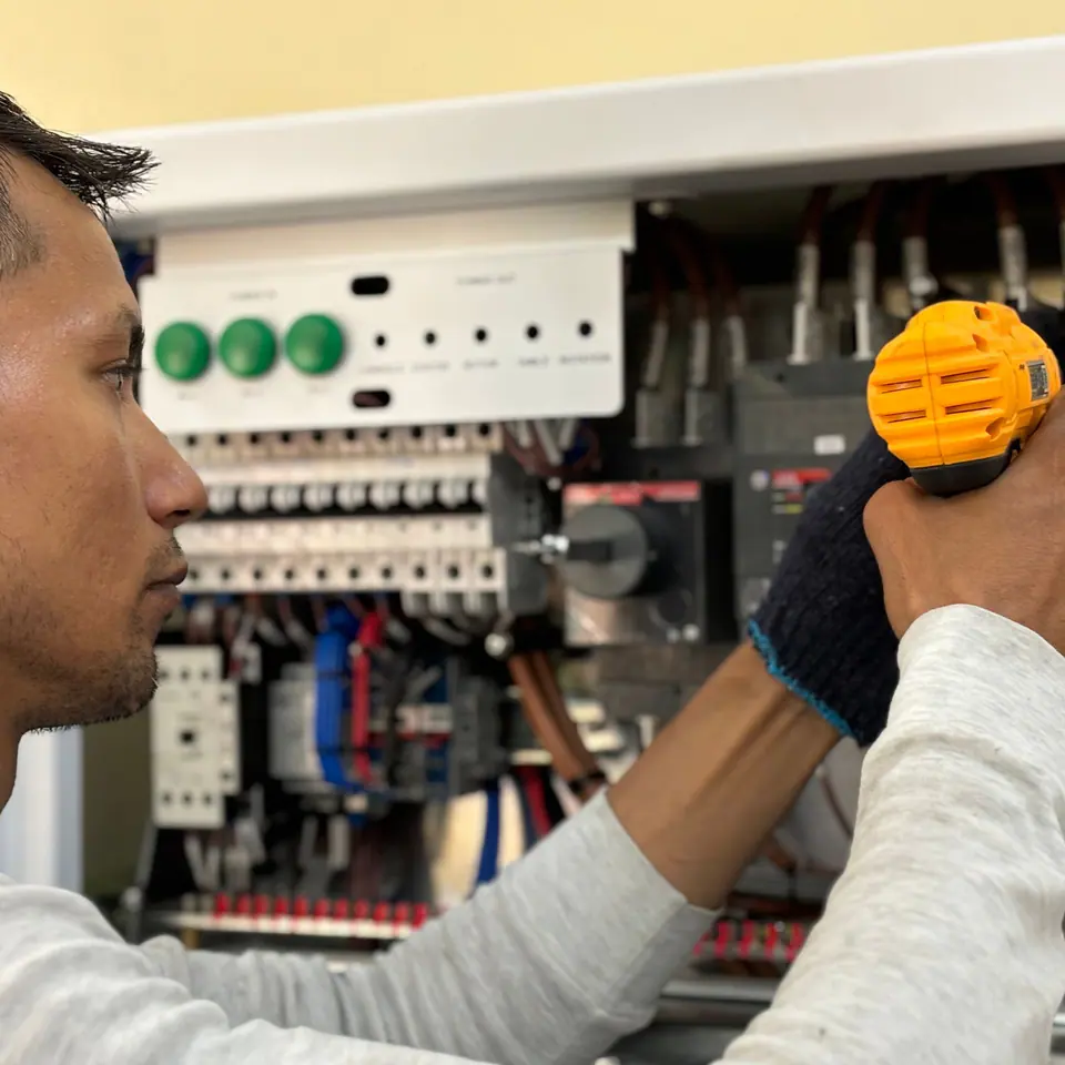 An electrician working inside an open electrical panel with a yellow power driver