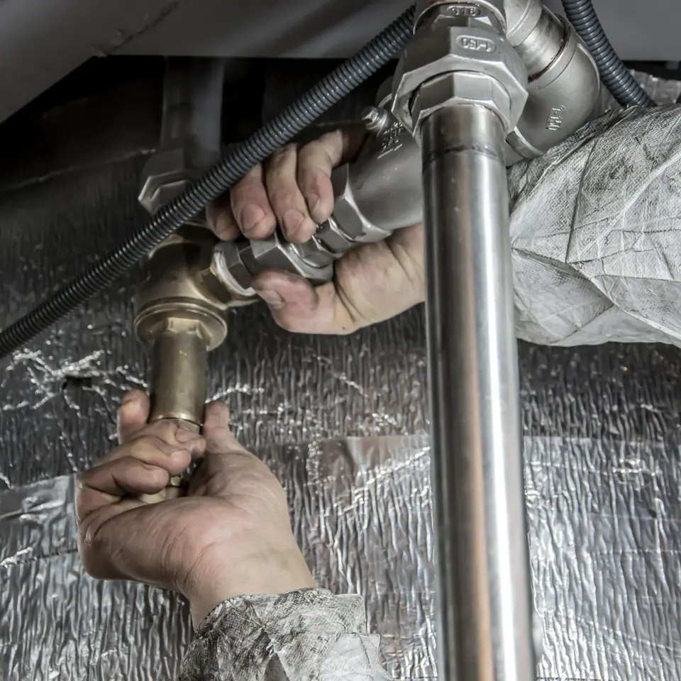 A plumber’s hands tightening steel pipe fittings with a wrench against foil insulation