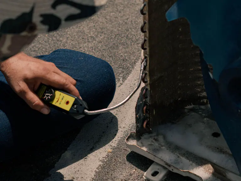 A technician connecting a refrigerant gauge to an outdoor air conditioning coil