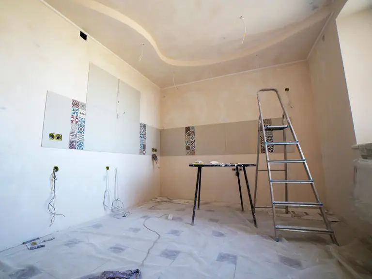 A room mid-renovation with a stepladder beside a wall of patterned accent tile over bare plaster
