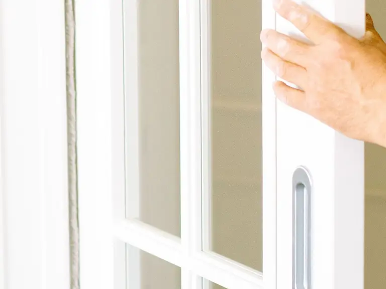 A hand reaching for the handle of a white French-pane sliding door, its glass panes and grille visible
